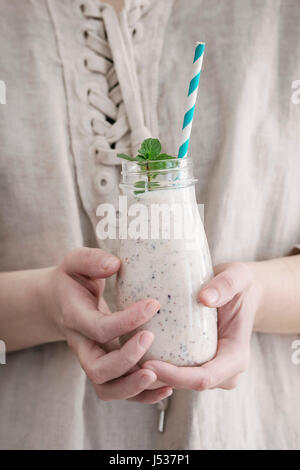 Eine Flasche Smoothie mit Chia-Samen, Heidelbeeren, Minze und retro gestreiftes cocktail Rohr in weiblichen Händen. Frau in weißem Leinen Kleid. Gesunde eati Stockfoto