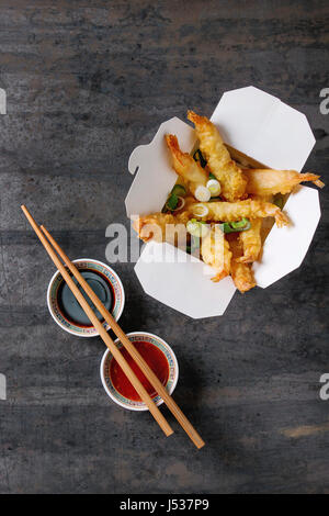 Fried-Tempura-Garnelen mit Reis und Frühlingszwiebeln in Pappschachtel zum mitnehmen. Serviert mit Saucen, Stäbchen über alte Metall Hintergrund. Ansicht von oben, Raum. Asiatische Stockfoto