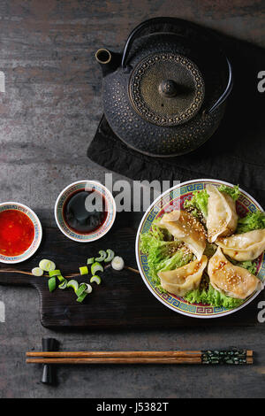 Gyozas Potstickers auf Eisbergsalat mit Saucen. Serviert im traditionellen Porzellanplatte mit Stäbchen und schwarz Teekanne auf Holz dienen Board über alte erfüllt Stockfoto