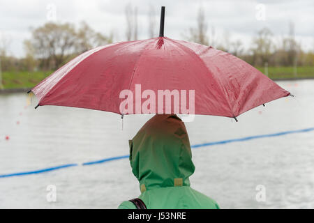 Jemand trägt einen grünen Regenmantel und hält einen roten Regenschirm an einem regnerischen Tag Stockfoto