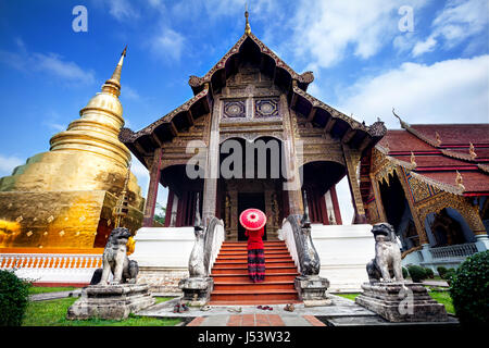 Frau Tourist mit roten traditionelle Thai Regenschirm in der Nähe von Golden Tempel Wat Phra Singh in Chiang Mai, Thailand Stockfoto