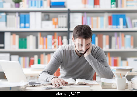 Young konzentrierte sich kluger Mann im Büro zu studieren und ein Buch lesen, Regale auf Hintergrund Stockfoto