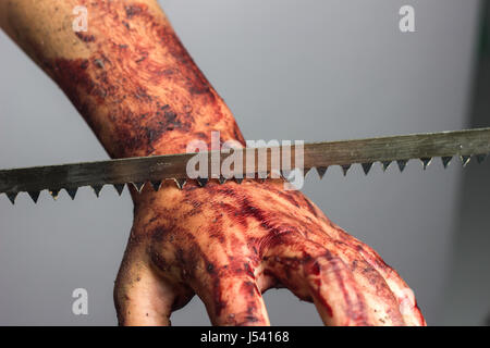 Schneiden in den blutigen Hand mit Sägeblatt vor grauem Hintergrund Stockfoto