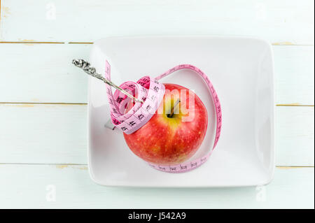 roter Apfel mit Maßband und Gabel auf hölzernen Hintergrund, Diät-Konzept Stockfoto