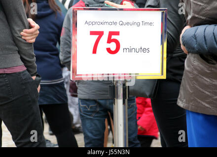 Menschen warten in einer langen Schlange, Fokus auf dem Hinweisschild. Plakat mit Informationen über die Wartezeit neben Linie mit vielen Menschen warten. Stockfoto