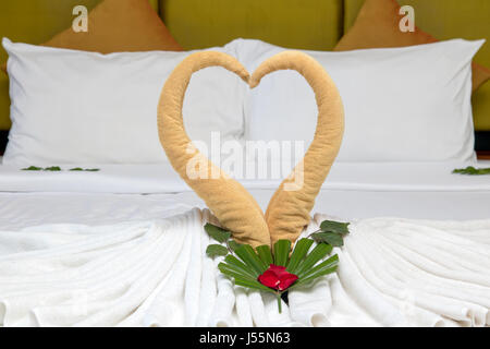 Handtuch wie Vögel Dekoration mit roten Rosenblättern auf weißen sauberen Bett im Hotelzimmer Stockfoto
