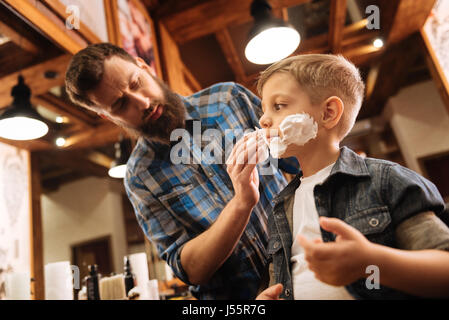 Gut gut aussehende Putten Schaum auf das Gesicht des jungen Barbier Stockfoto