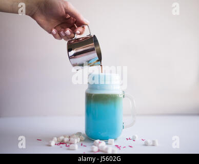 Frau ist Kaffee in stilisierten Einmachglas Tasse farbige blaue Milch gießen. Milch-Shake, Cocktaill, Frappuccino.  Einhorn Kaffee, Einhorngericht. Stockfoto