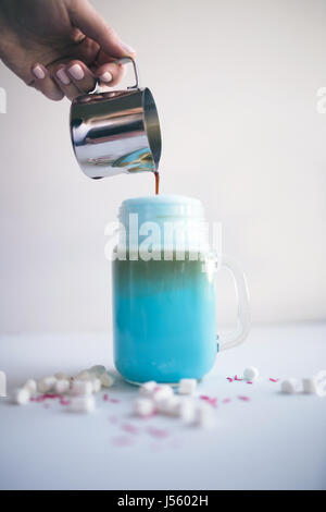Frau ist Kaffee in stilisierten Einmachglas Tasse farbige blaue Milch gießen. Milch-Shake, Cocktaill, Frappuccino.  Einhorn Kaffee, Einhorngericht. Stockfoto