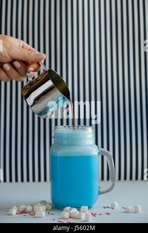 Frau gießt Kaffee in stilisierten Einmachglas Tasse farbige blaue Milch auf einem schwarz-weiß-Hintergrund. Milch-Shake, Cocktaill, Frappuccino.  Einhorn-c Stockfoto