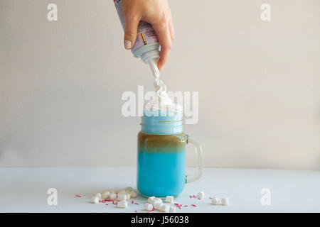Mädchen ist in stilisierten Einmachglas Tasse farbige blaue Milch Sahne hinzufügen. Milch-Shake, Cocktaill, Frappuccino.  Einhorn Kaffee, Einhorngericht. Stockfoto
