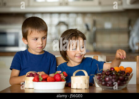 Zwei süße Kinder, junge Brüder essen frisches Obst zu Hause, Erdbeeren, Kirschen, Himbeeren, Heidelbeeren Stockfoto