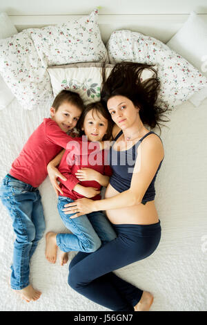 Schöne schwangere junge Mutter und ihre beiden Kinder, jungen, liegend im Bett zu Hause Stockfoto