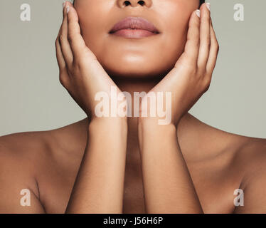 Schuss von junge Frau mit schönen und gesunden Haut zugeschnitten. Nahaufnahme von Weibchen berühren ihr frisches klares Gesicht vor grauem Hintergrund. Stockfoto