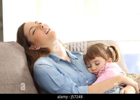 Erschöpfte Mutter umarmt Tochter schläft Baby sitzt auf dem Sofa zu Hause schlafen Stockfoto