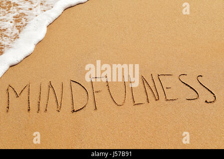 das Wort Achtsamkeit, geschrieben in den Sand des Strandes Stockfoto