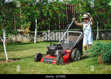 kleine niedlicher junge mäht Rasen mit Mäher Stockfoto