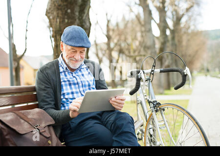 Ältere Mann in der Stadt sitzen auf Bank, arbeitet an tablet Stockfoto