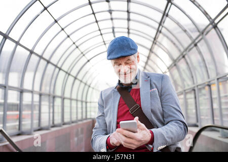 Ältere Mann mit Smartphone gegen Glas Decke SMS. Stockfoto