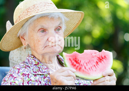 Gerne ältere Frau essen Wassermelone im Garten Stockfoto