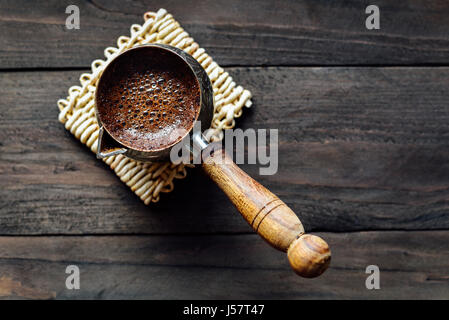 Frisch gebrühter Kaffee in türkischen Cezve mit Schaum auf hölzernen Hintergrund Stockfoto