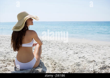 Rückansicht der Trägerin Sonnenhut beim Sitzen am Strand Stockfoto