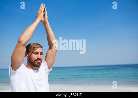 Mann mit den Händen umklammert Ausübung am Strand gegen blauen Himmel Stockfoto