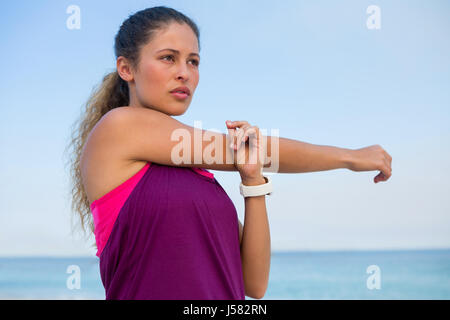 Nachdenkliche junge Frau stretching am Strand gegen klarer blauen Himmel Stockfoto