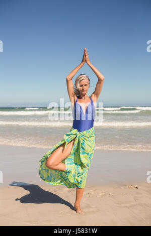 Ältere Frau praktizieren Yoga stehend gegen Meer am Strand Stockfoto