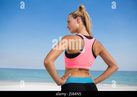 Rückansicht des Frau mit Hand im hip stehen am Strand gegen blauen Himmel Stockfoto