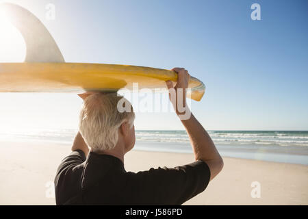 Rückansicht des senior Mann mit Surfbrett auf Kopf am Strand im sonnigen Tag Stockfoto