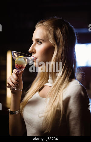 Seitenansicht des nachdenklichen Frau trinkt Martini stehend in Nachtclub Stockfoto