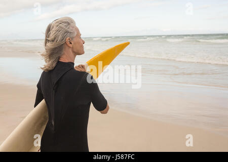 Seitenansicht der Frau mit Surfbrett stehend am Ufer am Strand Stockfoto