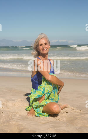 Porträt der lächelnde Frau, die Yoga praktizieren, sitzend auf Sand am Strand Stockfoto