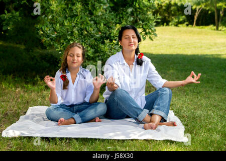 Bildern Sie Mutter und Tochter, Meditation, sitzen auf dem Rasen im Park von Stockfoto