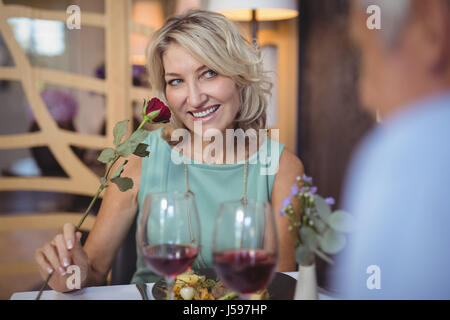 Reife Frau riechen eine Rosenblüte im restaurant Stockfoto