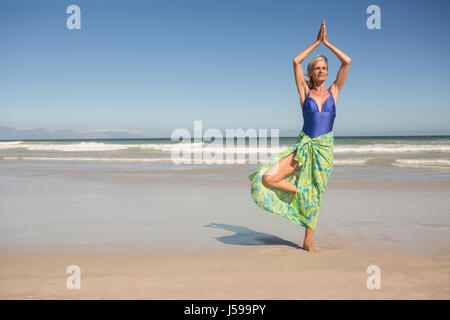 Ältere Frau praktizieren Yoga stehend gegen klaren Himmel am Strand Stockfoto