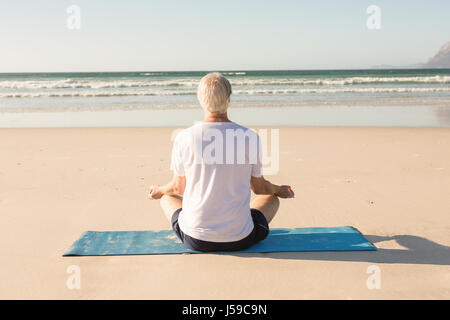 Ansicht der Rückseite des älteren Menschen meditieren am Strand Stockfoto