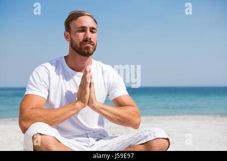 Mann sitzt im Gebet Position während des Trainings am Strand Stockfoto