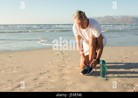 Ältere Mann binden Schnürsenkel am Strand gegen klaren Himmel Stockfoto