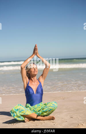 Ältere Frau, die Yoga praktizieren, während der Sitzung gegen Meer am Strand Stockfoto