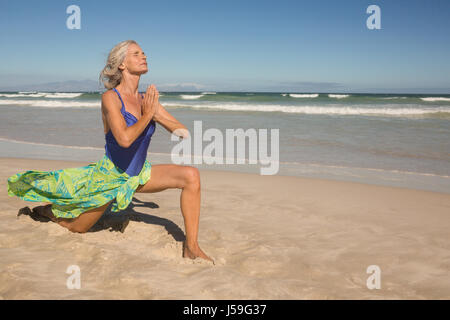 Ältere Frau praktizieren Yoga am Sand am Strand Stockfoto
