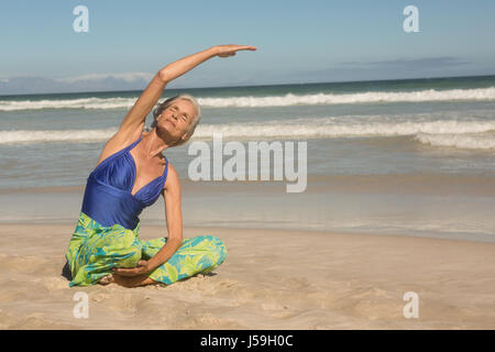 Ältere Frau, die Yoga praktizieren, während Sie auf Sand am Strand sitzen hautnah Stockfoto