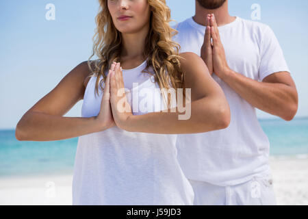 Mittelteil des Paares im Gebet Position Ausübung im stehen am Strand Stockfoto