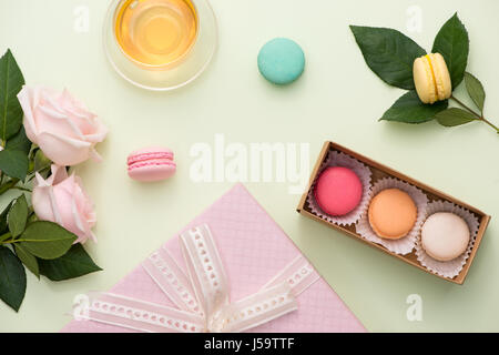 Französische Makronen. Viele süße bunte Macarons in Box mit Blumenstrauß aus Rosen auf dem Tisch Stockfoto