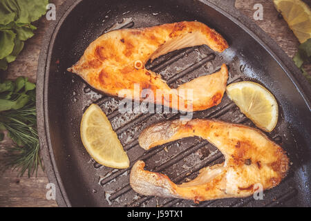 Gebackene Steak Forellen Fischen in gusseisernen Form, rund um die Grüns, Blätter, Salat, Zitrone, Olivenöl, Pfeffer, Gewürze. Von oben, Nahaufnahme. Konzept der healt Stockfoto