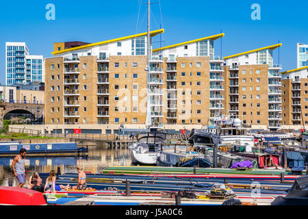 London, UK - 8. April 2017 - Leute zum Sonnenbaden auf den Booten vertäut am Limehouse Bassin mit Wohnungen im Hintergrund Stockfoto