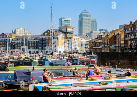 London, UK - 8. April 2017 - Leute zum Sonnenbaden auf den Booten vertäut am Limehouse Bassin mit Canary Wharf im Hintergrund Stockfoto