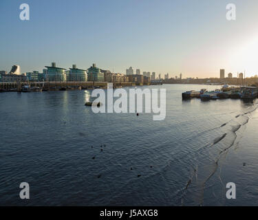 Die Sonne geht über einen ruhigen Themse mit Canary Wharf im Hintergrund, London, England UK Stockfoto