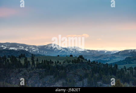 Panoramische Ansicht der Sonnenaufgang über dem schneebedeckten, schroffe Berge mit kleineren felsigen Hügeln im Vordergrund. Fotografiert bei Tageslicht im Yellowstone Stockfoto